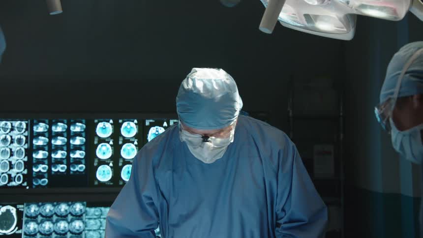 Team of surgeons in a room with one of them taking a scalpel and preparing to perform a surgical procedure