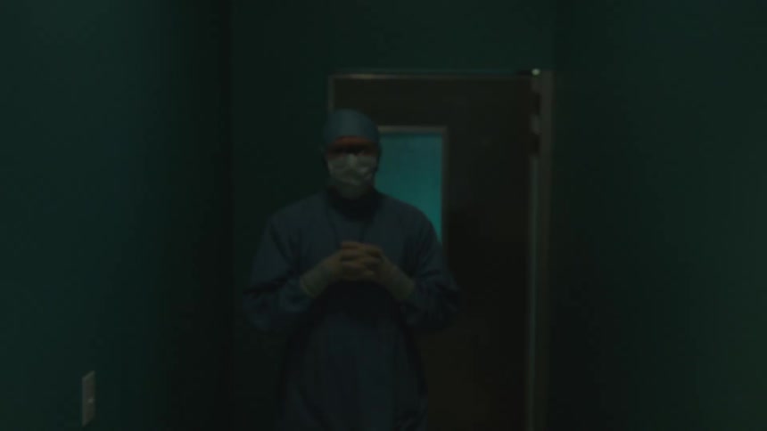 A surgeon walks through a hospital door and unclasps his hands
