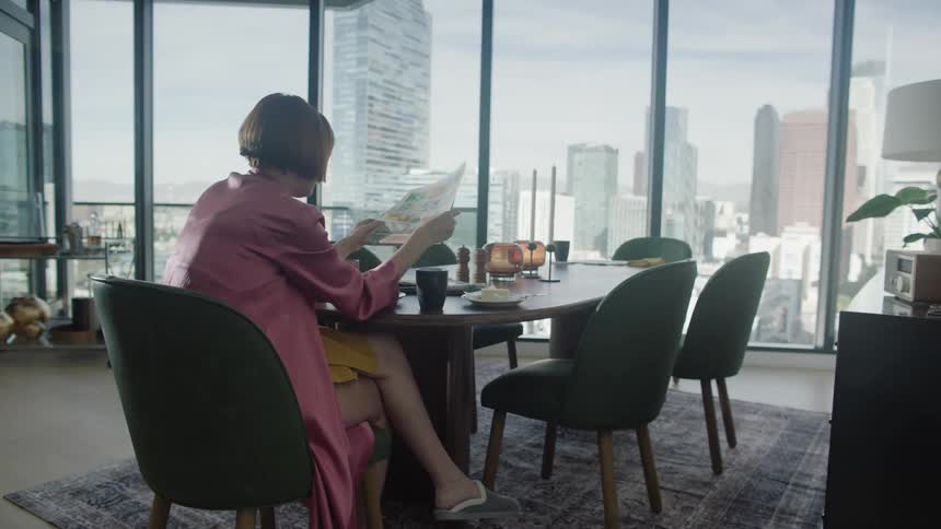 Woman sitting at the table drinking a cup and reading a newspaper with a panoramic view of a metropolis with a skyscraper