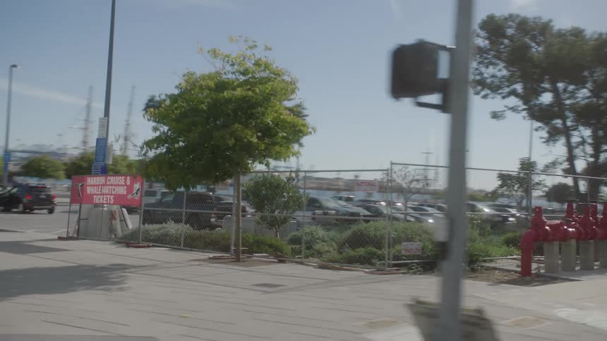 View from the window of a moving vehicle of a parked orange bus and a parking lot with several private vehicles