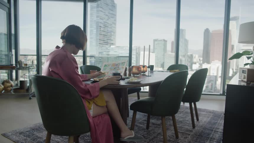 A woman sits at a dining table and eats breakfast in a highrise apartment building