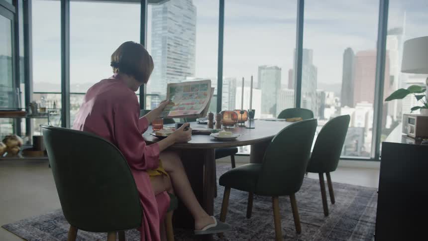 Woman sitting at a table reading a newspaper and with a panoramic view of a metropolis with skyscrapers