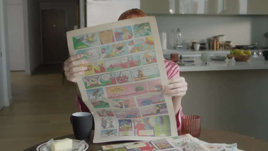 Woman sitting at the table reading comics in a newspaper