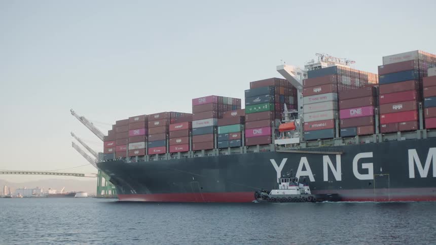 The yang ming cargo ship is being escorted by a tugboat as it transports freight