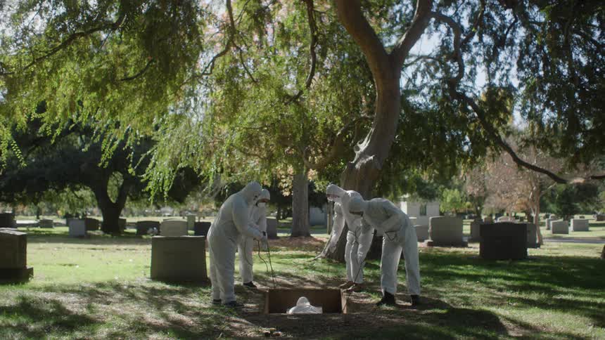 Four people in white protective clothing burying a body in the cemetery
