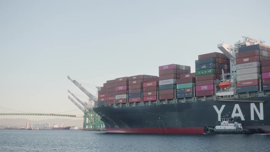 Container ship moves past loading dock with a bridge in the background