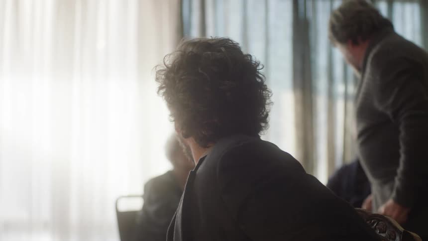 A man watches while another man angrily talks to an elderly woman