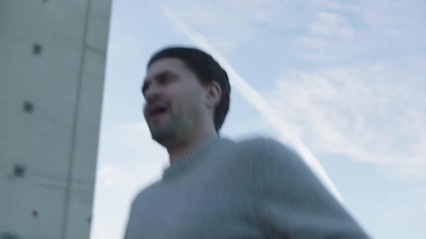 A man wearing a gray sweater jogs in the street past an apartment building