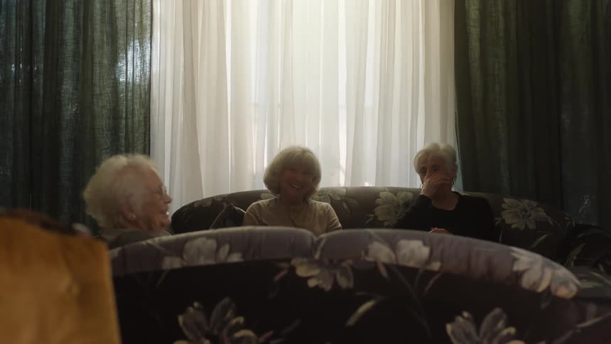 Three elderly women have a laugh in a living room