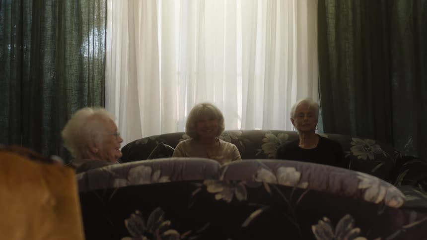 Three old women sit on couches laughing together