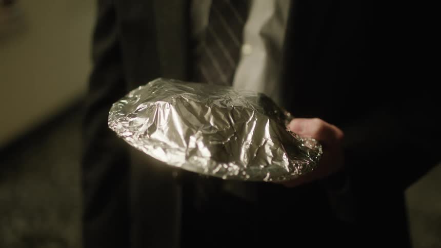 An object wrapped in aluminum foil held by a hand of a person who is wearing a suit with a tie