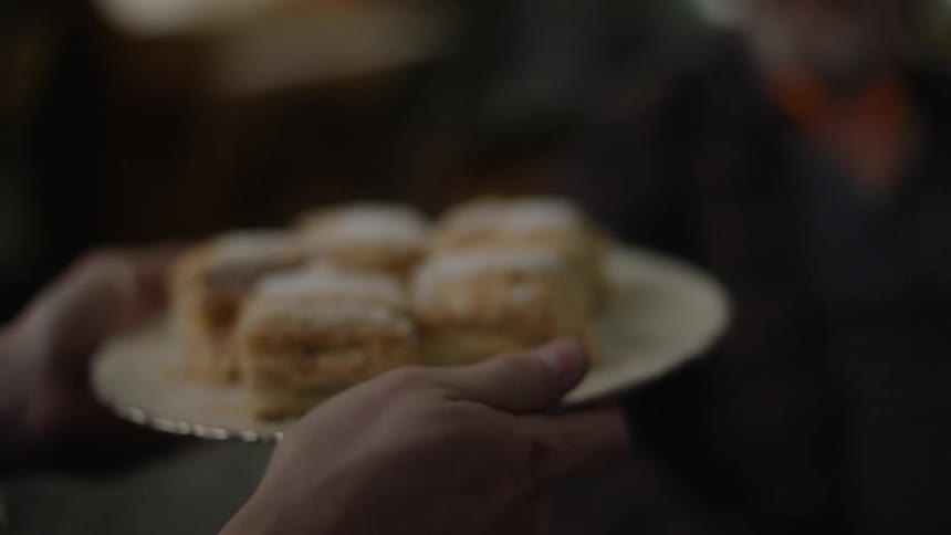 A person hands a plate of cake to an old woman