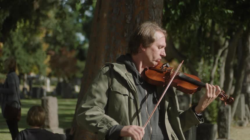 A man is playing the violin in the graveyard