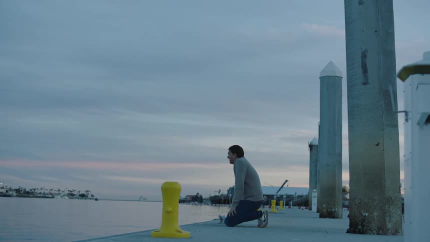 A man jogs over to the shore and kneels down to rest