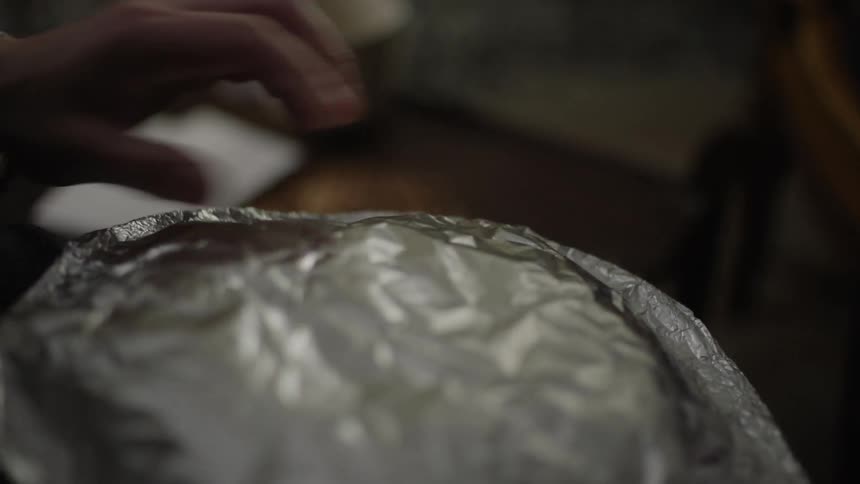 Hands of a person taking an aluminum foil off a plate with cakes