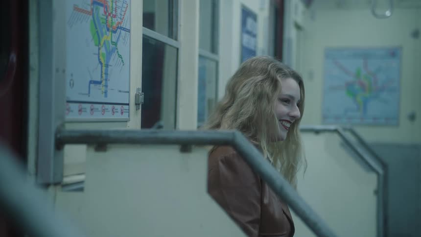 A blonde woman is smiling and they are sitting on a subway bench