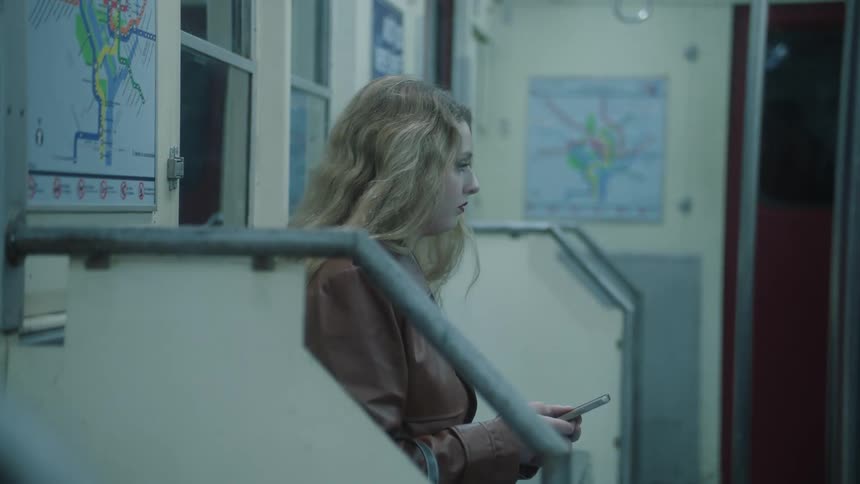 A blonde woman uses a smartphone on a subway car