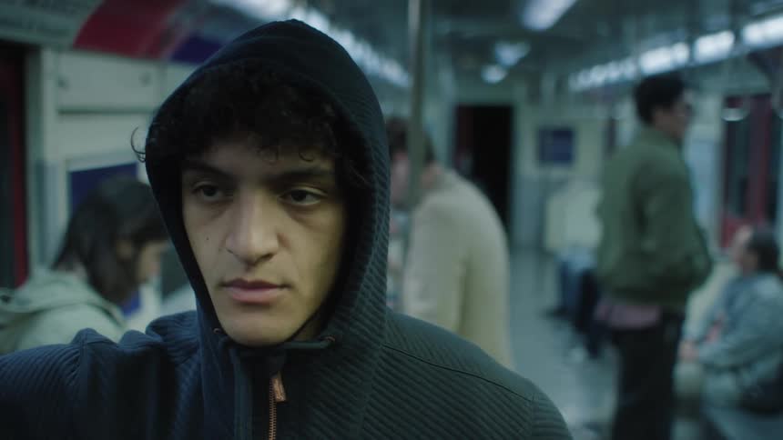 The face of a man who is wearing a hood and is standing in a subway