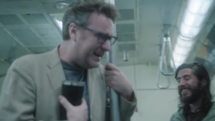 Two men within a meter are laughing and one of them is holding an iron pipe
