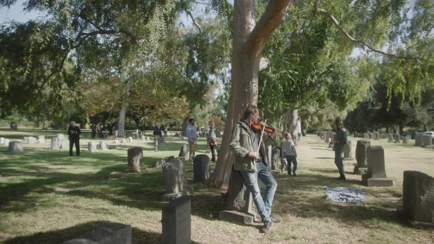 Musician playing a violin in a cemetery with people around