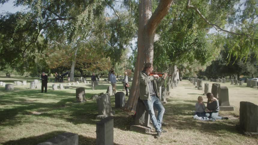 Family has a picnic in the cemetery while male violinist plays nearby