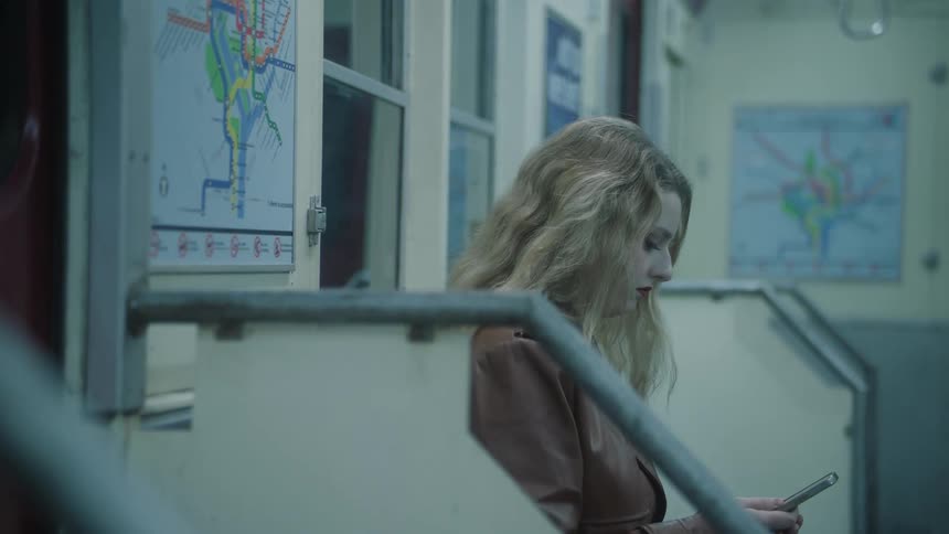 Blonde woman wearing a brown leather jacket uses a smartphone while traveling by subway