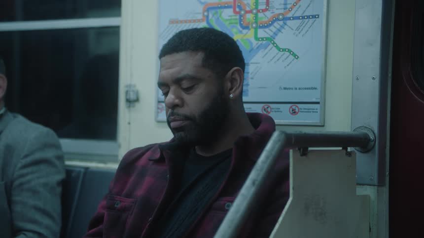 A man is sitting on a subway seat and he is looking down