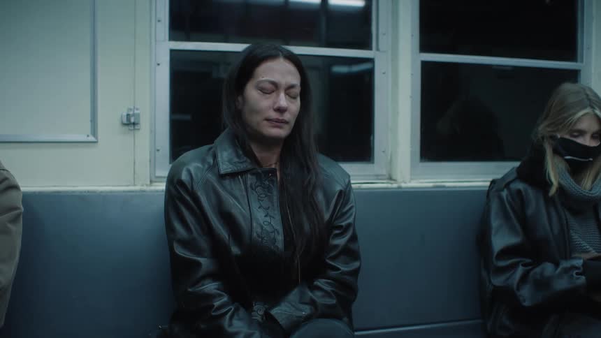 Woman sitting on a train bench with passengers around and she is crying