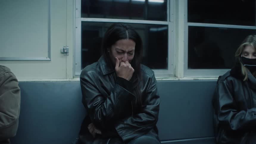 A woman is sitting on a subway bench and she is crying a lot and puts her hand over her mouth