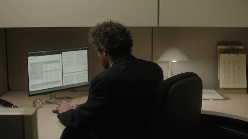 Man sitting at an office desk typing on computer and analyzing