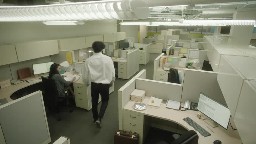 Male office worker stands and walks between cubicles to talk to coworker
