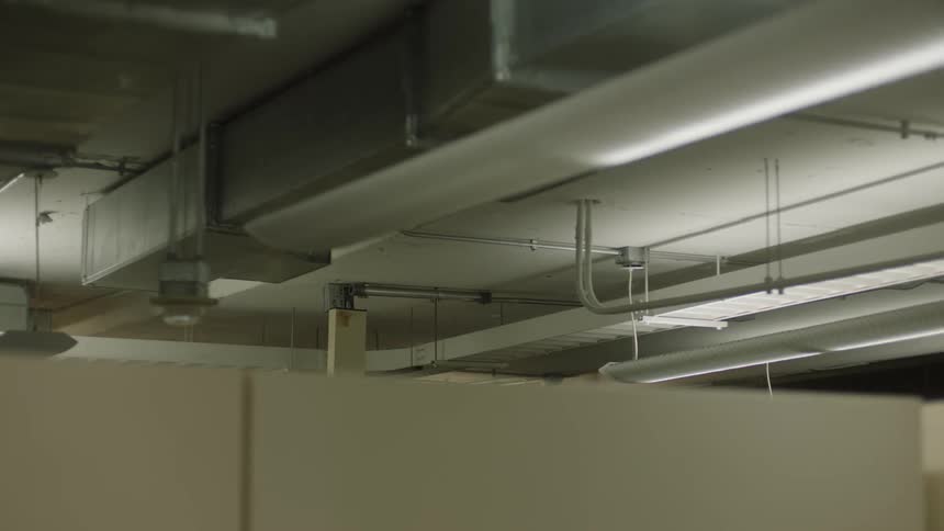Wooden booths with partitions in an office with a ceiling with pipes and light illuminating the environment