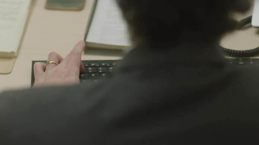 The hands of a person with their back turned and typing on a black keyboard