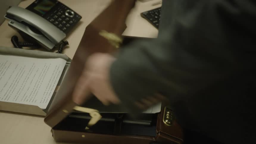 Male office worker places file in briefcase then closes it