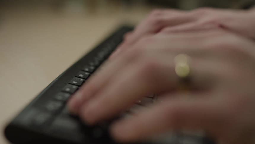 Hands of a person with a golden ring typing on a keyboard