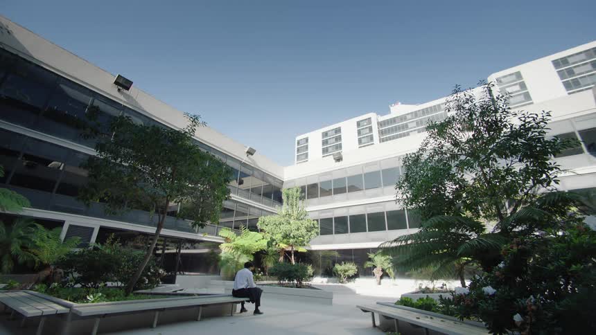 Man sitting on a bench in an openair environment with buildings around in daylight