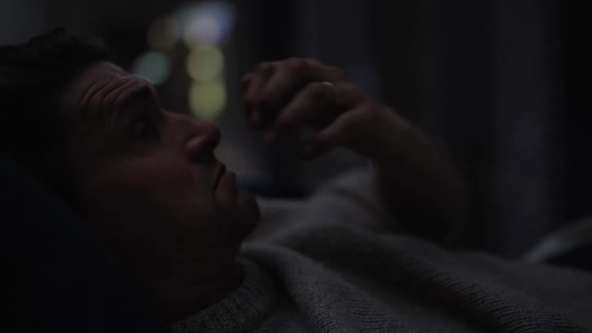 A tired man rubbing his face with his hands in bed