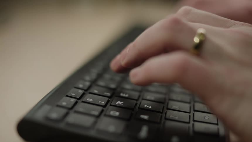 A human hand with a golden ring is typing on a black keyboard