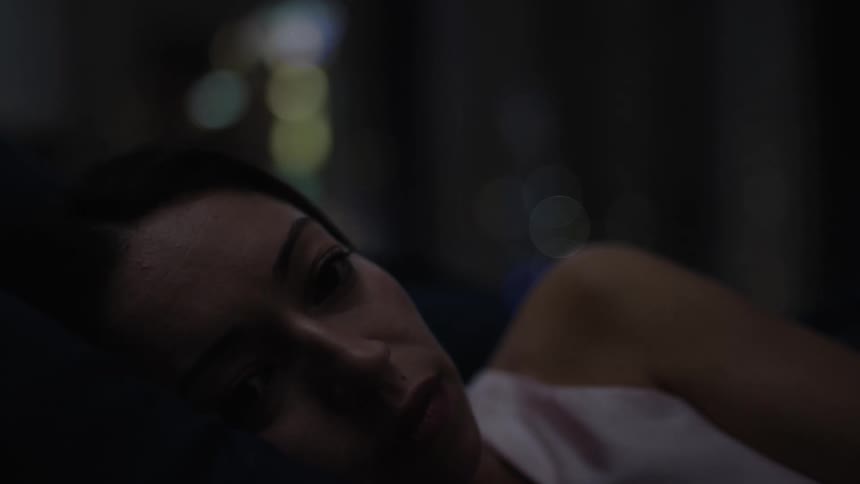 A woman in a white shirt lies in bed to sleep in the bedroom