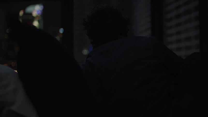 A silhouette of a person who is only on his back and lying down and he is looking at a building