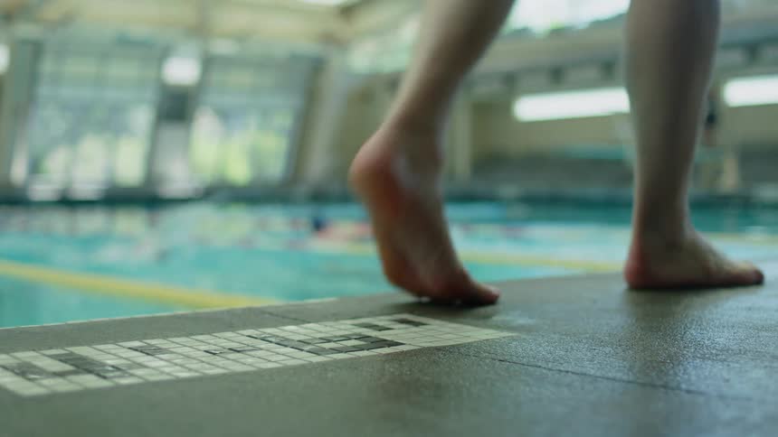 People swimming in the lanes of a pool and a persons feet passing by