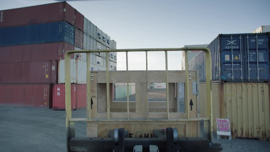 A forklift moves through stacks of shipping containers