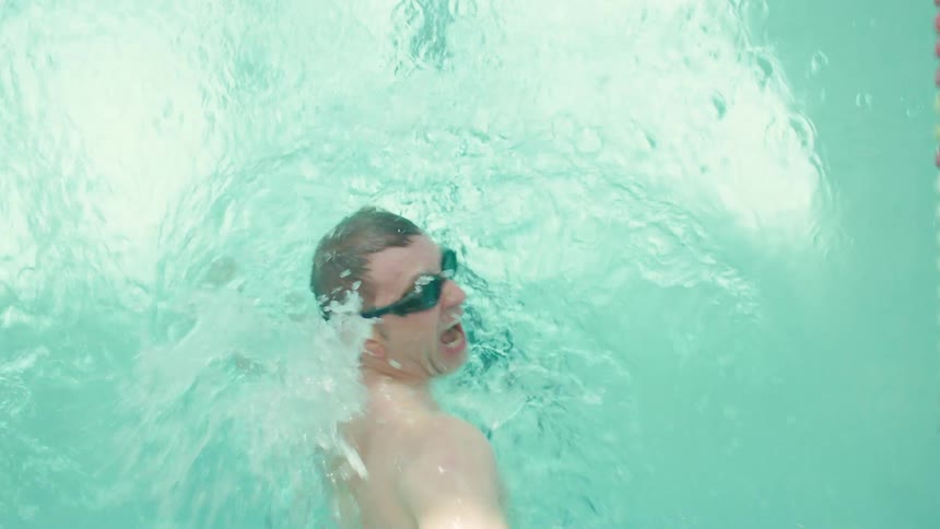 Man wearing goggles and swimming shorts swims in the water of an olympic swimming pool
