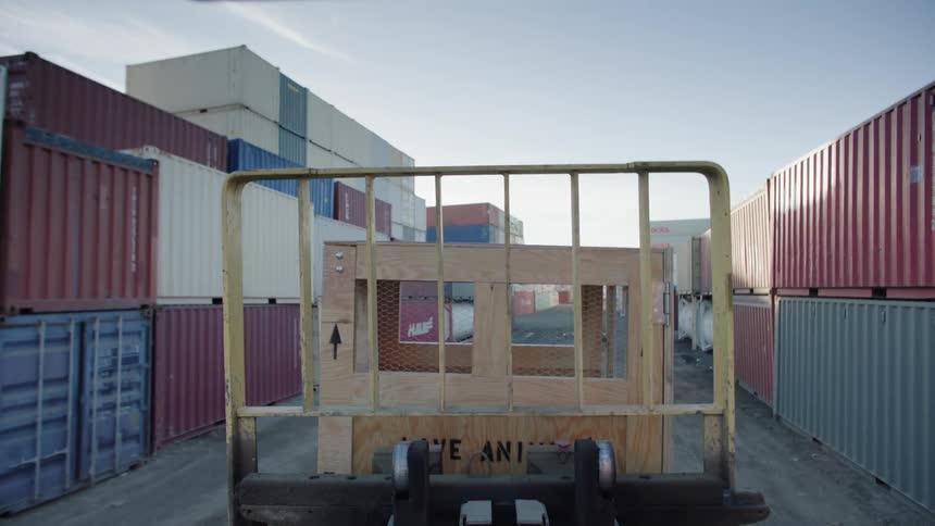 A wooden box with a crate is being transported by a vehicle on a path full of containers