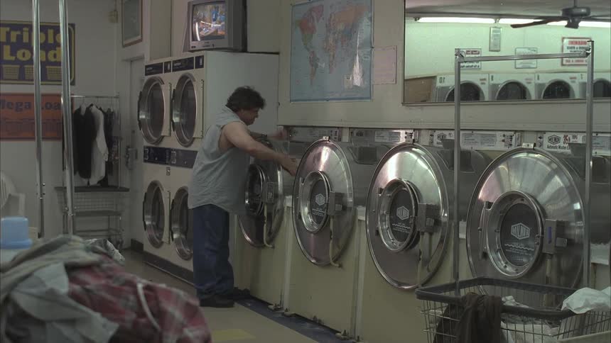 An angry man kicks and hits a washing machine in a laundromat