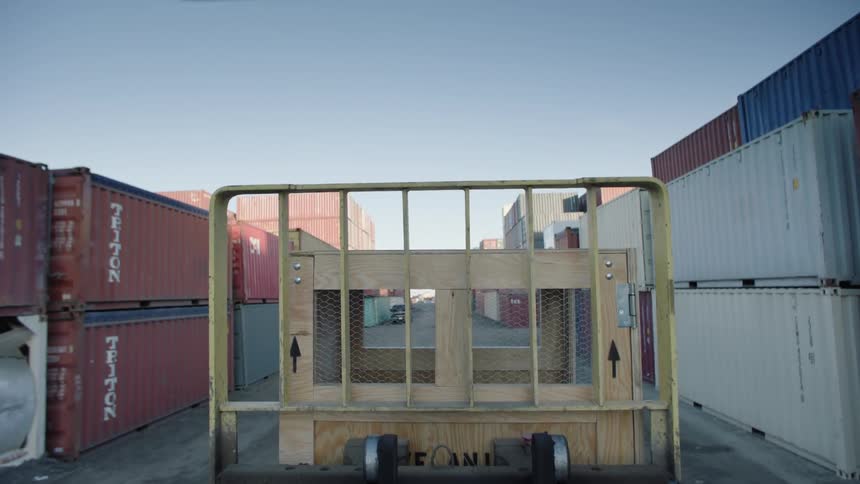 A wooden box with a crate and is being transported by a vehicle with a yellow crate on a path full of containers