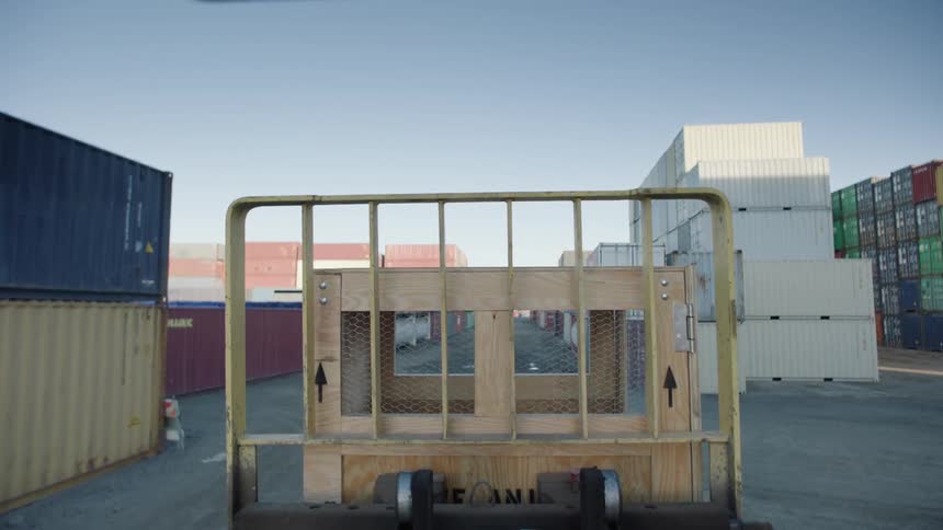 A forklift transports a wooden crate in a shipyard on a sunny day