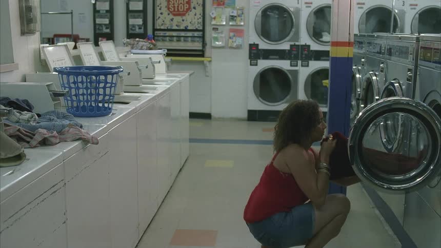 A woman in a laundromat takes her clothes from a washing machine