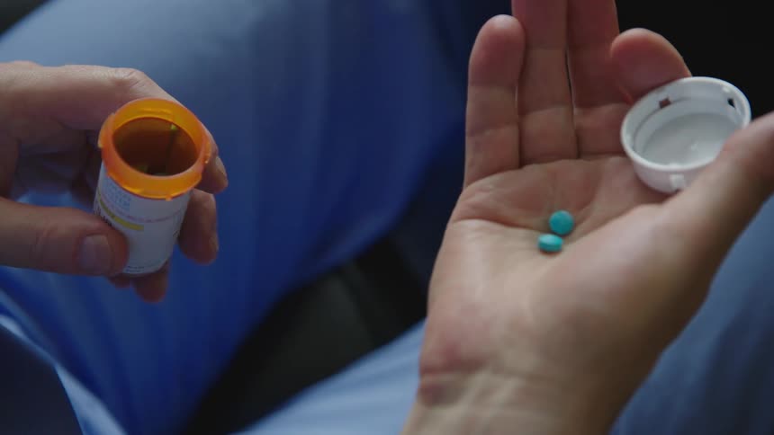 A person holds two pills in a shaking hand