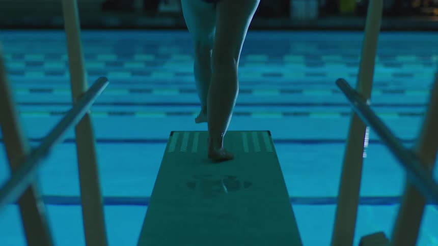 Legs of a woman jumping towards an illuminated pool at night